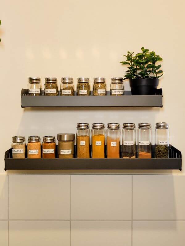 Gewürze wurden umgefüllt in einheitliche Gläser und stehen auf zwei Gewürzregalen, die an der Wand hängen.